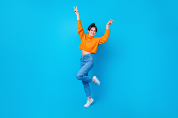 Full length photo of carefree cheerful woman dressed orange sweater rising arms showing v-signs...