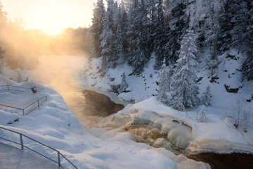 Kivach waterfall in winter in the light of the bright sun.. The fast flow of a winter forest river on a frosty day.