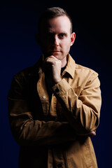 Portrait of a confident man on a dark background in a brown shirt. The emotion of concentration. A man without a smile
