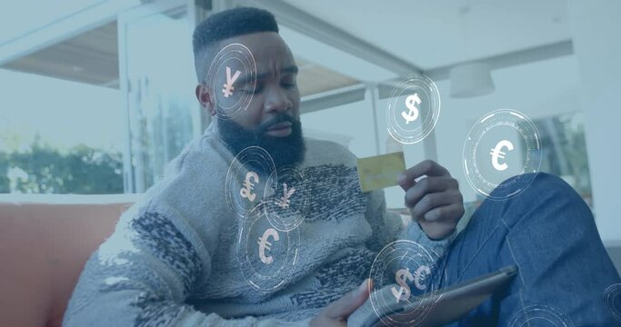 Animation of currency icons and data over african american man paying online with card