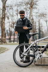 A modern and stylish businessman using a tablet outdoors, standing next to his bicycle in a park setting.