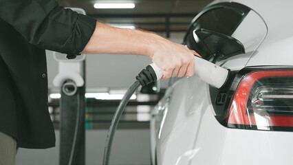 Young man travel with EV electric car to shopping center parking lot charging station in downtown...