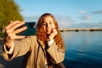 Happy woman with a mobile phone, takes a selfie, communicates with friends, blogs outdoor....