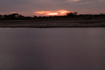Long exposure shot of Corriente river in Esquina, Corrientes, Argentina, at sunset. Beautiful blurred water effect, dramatic clouds and hiding sun at nightfall.	