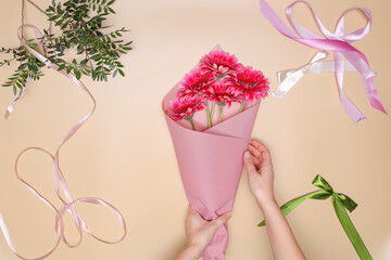 florist makes a bouquet of pink gerberas. girl wraps flowers in paper on workspace. top view, flat lay