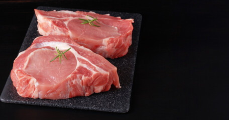 Raw pork steak with rosemary on a black table
