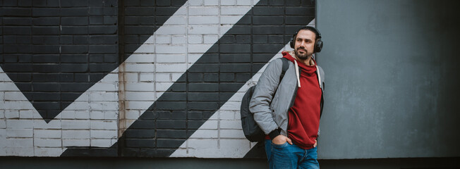 Portrait of a young man wearing headphones on a city background, against a wall with a geometric pattern.