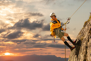 woman climbing in the mountain at sunset with lus rays, security, confidence business woman, rope access, life insurance.
