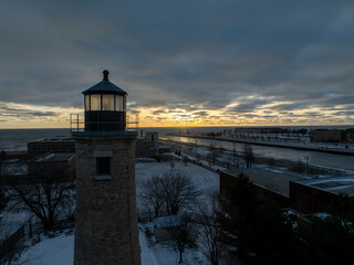 Historic lighthouse at dusk with a second lighthouse in the near distance overlooking a snow-covered landscape and harbor on Lake Michigan.