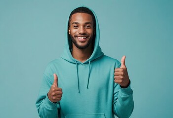 A casual man in a teal hoodie gives double thumbs up, his smile exuding friendliness and approachability. - obrazy, fototapety, plakaty