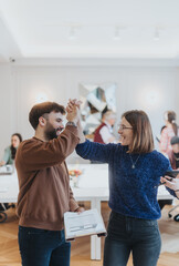 Joyful professional interaction captured as two colleagues high-five in a well-lit office setting,...