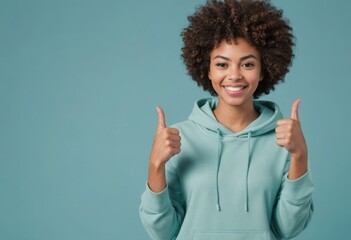 A happy woman in a hoodie giving double thumbs up. Her joyful expression radiates happiness and casual style. - obrazy, fototapety, plakaty