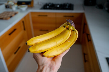 Man's hand holding bananas, natural daylight in the wooden kitchen