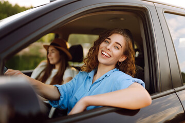 Two trendy attractive young woman singing along to the music as they drive along in the car through...