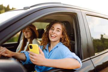 Two trendy attractive young woman singing along to the music as they drive along in the car through...