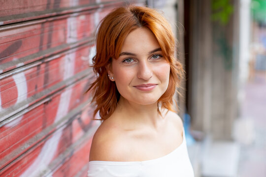 portrait of smiling young redhead woman, leaning on red garage shutter