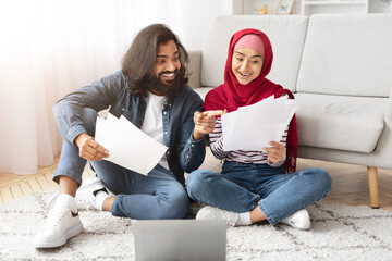 Happy young muslim couple checking documents while sitting on floor at home