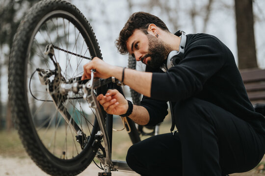 A dedicated businessman in casual attire kneels down to fix his bicycle in a tranquil outdoor setting, demonstrating versatility and hands-on ability.