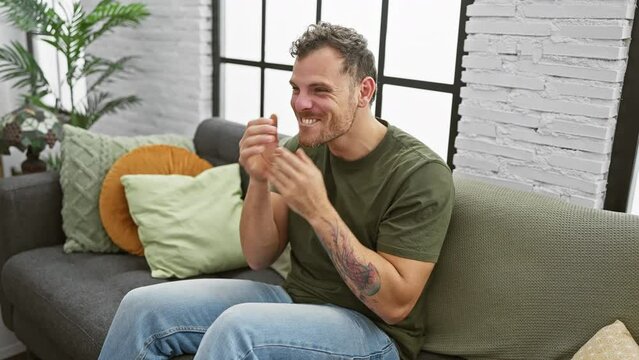 Cheerful young man celebrating joyful win on sofa at home, sporting a winner's smile and victory expression
