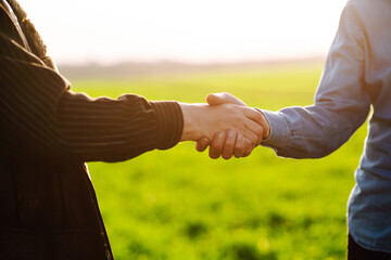 Farmer's handshake against the backdrop of a green wheat field. Successful deal. Agriculture and business concept.