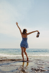 A woman dances freely on the beach, her dress and hair swept up in the invigorating sea breeze
