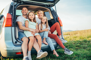 Portrait of Happy young couple with little daughters sitting inside car trunk during auto trop....
