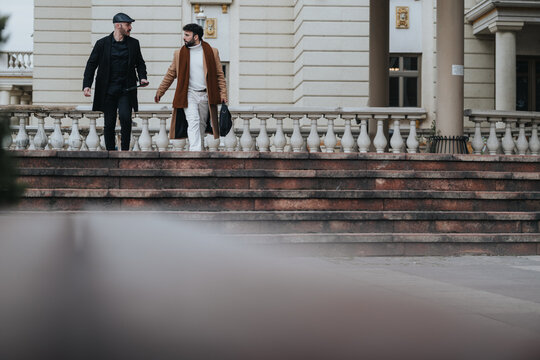 Image of two stylish adult men engaged in conversation while walking down the steps of an elegant city building, reflecting urban lifestyle and friendship.