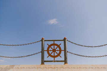 A vivid image capturing a ship's wheel mounted above a railing, set against a clear blue sky