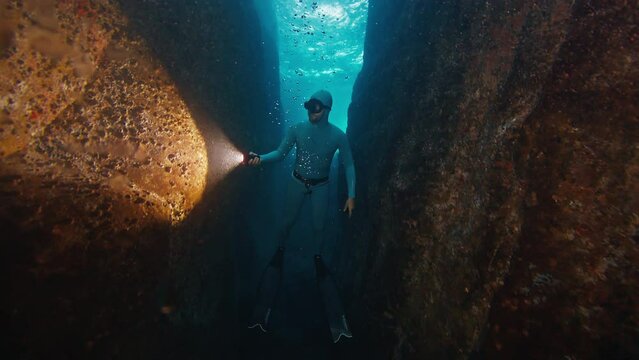 Freediver swims underwater in the sea. Man freediver floats in the underwater canyon and explores it with torch