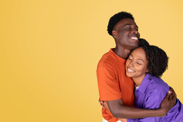 A content young woman in a purple blouse embraces a joyful young man in an orange shirt