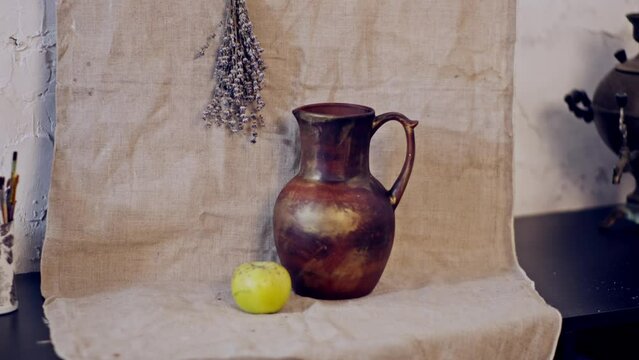 Artistic still life with a jug, apple and a bunch of lavender on a canvas. Still life painting on the table in the art workshop.  