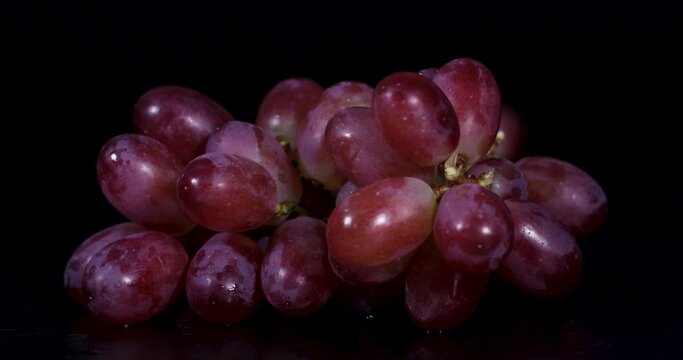slow motion of falling grapes. luster of plump, ripe red grapes with a slight purple hue, displayed against a black background.