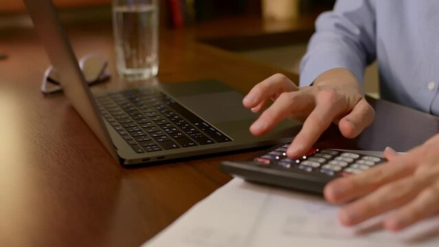 Close-up video of young woman using calculator and laptop to summarize monthly incomes and outcomes. Checks her electronic bills, payments in e-banking application and manages household finances.