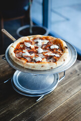 Appetizing Italian pizza with cheese and meat on a metal stand.