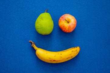 Smile from fruits – banana, apple and pear. Blue mat in background