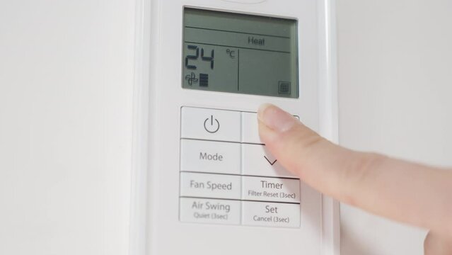 Remote control for the air conditioner on a white wall, a woman turns it on and increases the temperature to the maximum in heating mode.