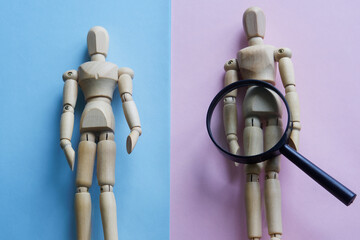 Wooden mannequins and magnifying glass on pink and blue. The theme of gender identity and...
