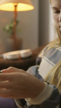 A hipster girl sits in a room, setting aside her phone and picking up a book. The video is taken from the side, capturing the transition from digital interaction to analog engagement,Vertical