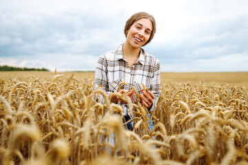 Young female farmer in her hands  in a wheat field checks the quality and growth of the crop. Harvesting. Agro business.