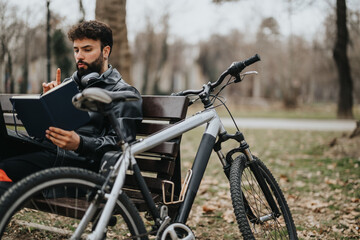 Entrepreneurial male business associate working remotely in a park, sitting on a bench with his bicycle beside him.