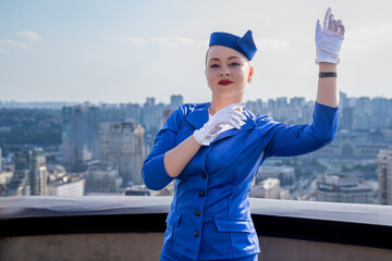 woman stewardess in blue vintage uniform with hat and gloves poses on roof. Flight attendant in...