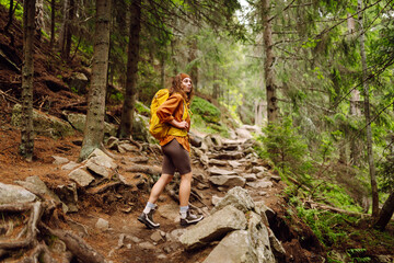 Naklejka na ściany i meble Beautiful traveling woman in the mountains on a background of a forest. Hiking, active lifestyle. Outdoor recreation concept.
