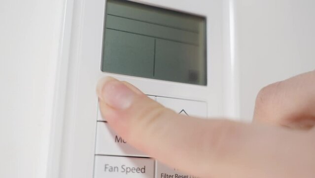 Close-up of the white air conditioner remote control on the wall, the woman lowers the temperature and turns it off.