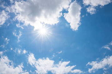 blue sky with bright sun and rays, white cumulus clouds around