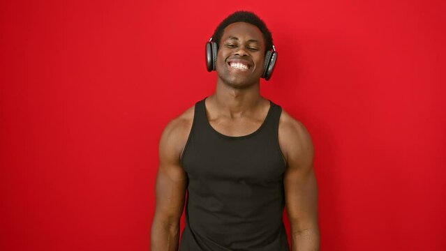 Cheery young african american man bopping to music, rocking a toothy, confident smile over isolated red wall, radiates happiness.