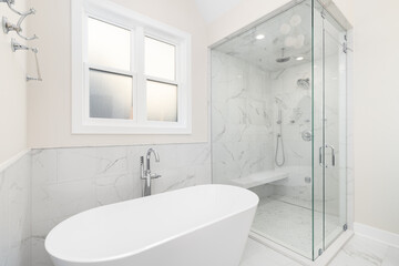 A bathroom's freestanding tub with a chrome faucet, marble tile on the walls and floor, and a...
