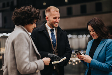 Business colleagues sharing laugh while checking smart phone outdoors.
