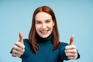 Smiling ginger woman with braces showing thumbs up gesture isolated