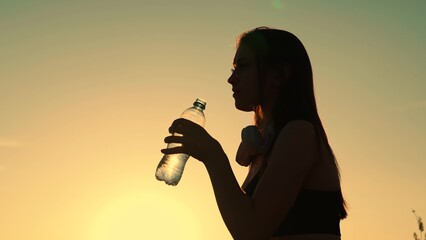 Beautiful young woman drinks water from bottle after outdoor sports workout. Girl with headphones...
