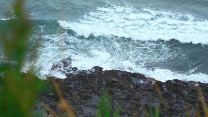 Close-up of surge of waves on rocky shore. Clip. Beautiful waves with splash roll on stones of seashore. Beautiful splashes of waves crashing on rocks on cloudy day